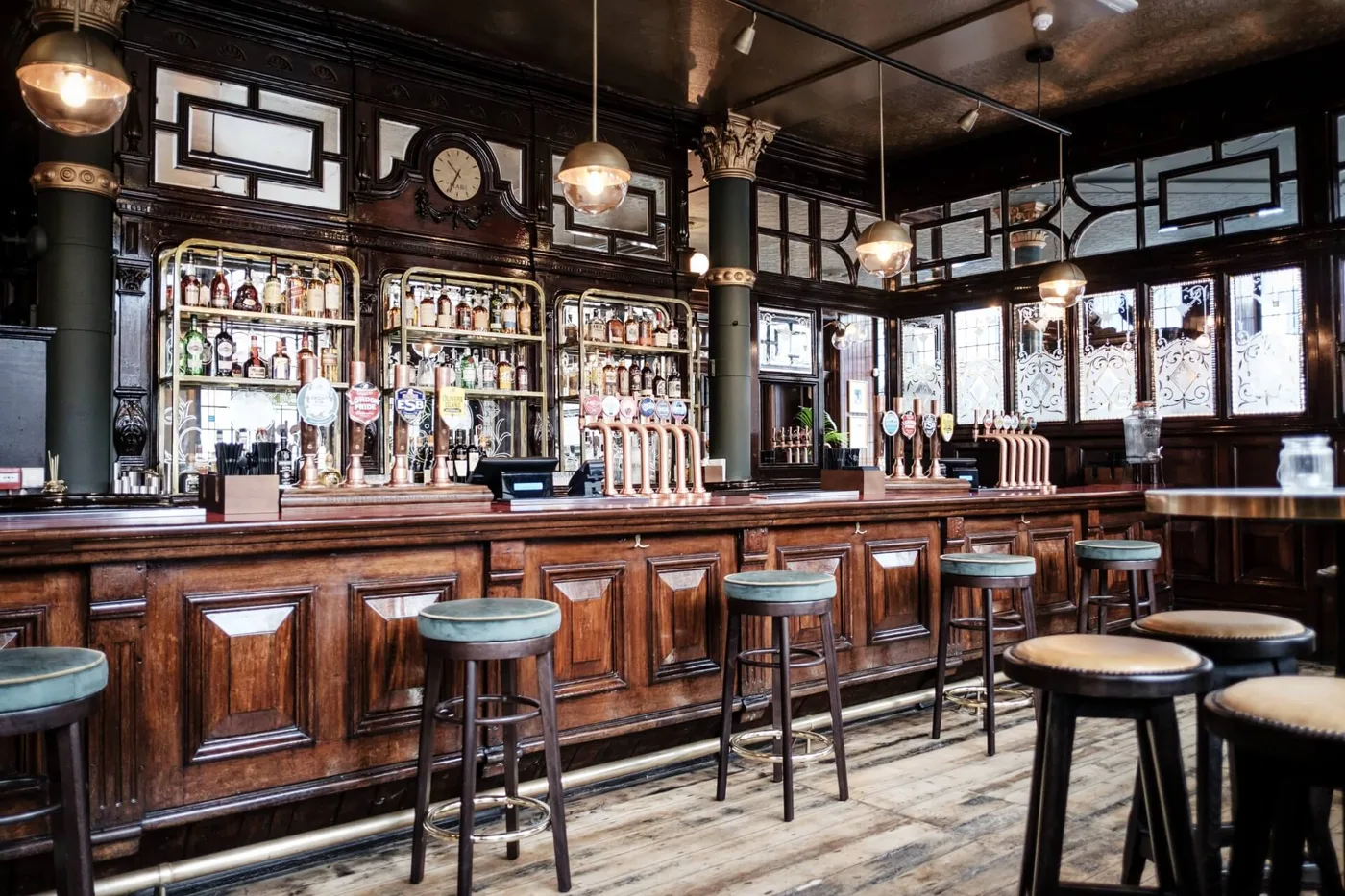 The long wooden bar inside The Half Moon, Herne Hill, with bar stools, brass pumps and etched glass windows